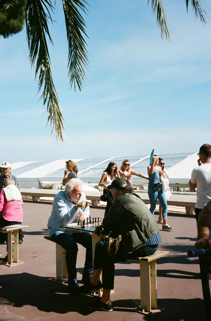 People enjoying leisure time with a chess game outdoors in a sunny seaside location.