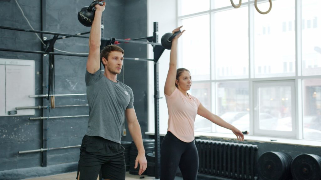 Man and woman performing kettlebell swings in gym
